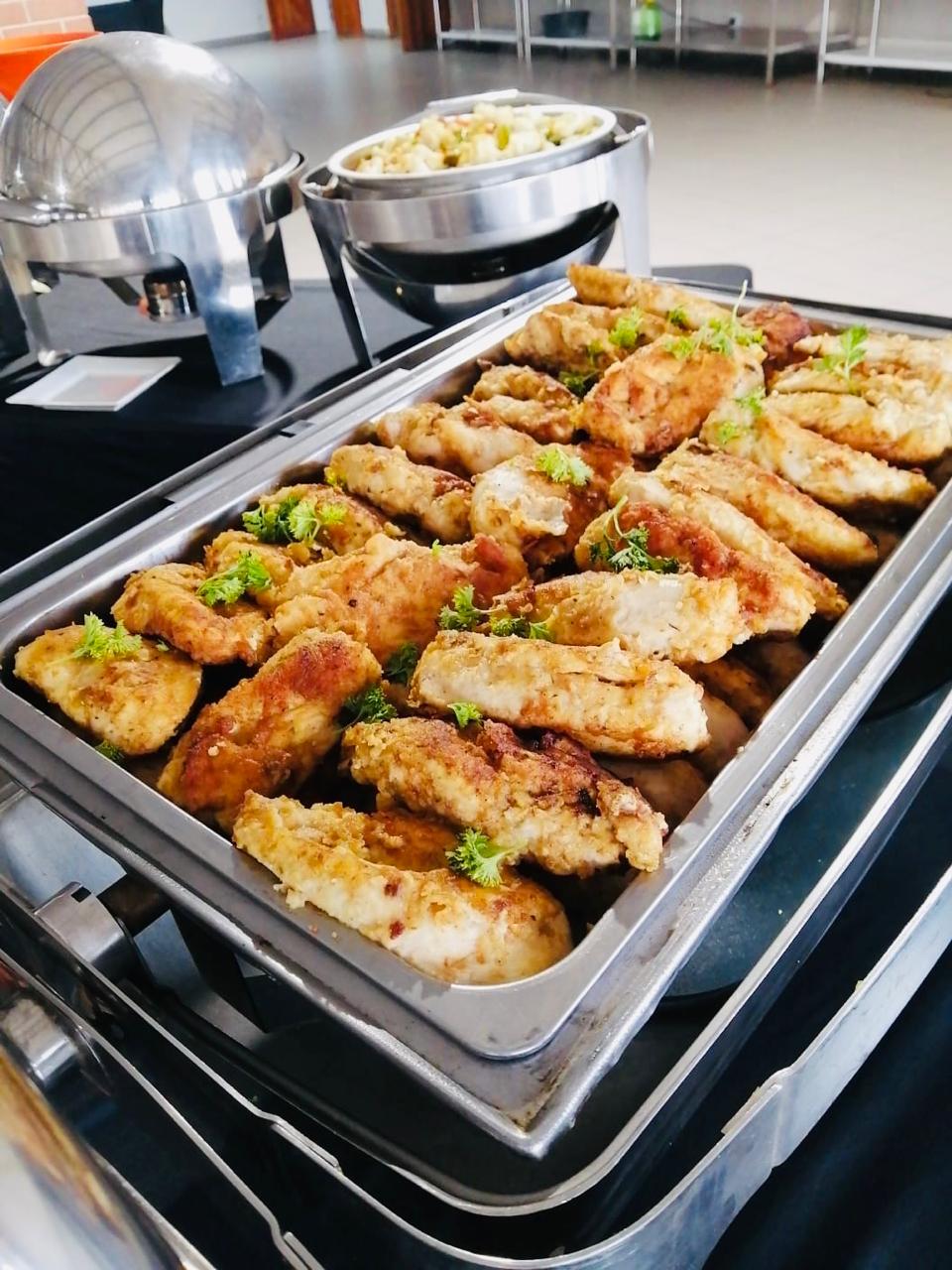 A chafing tray of crumbed chicken portions garnished with parsley on a set service line.