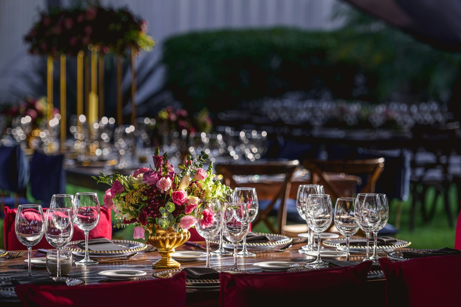 An evening event tablescape with wine glasses, red velvet chairs, gold candelabra and a fresh floral centrepiece.