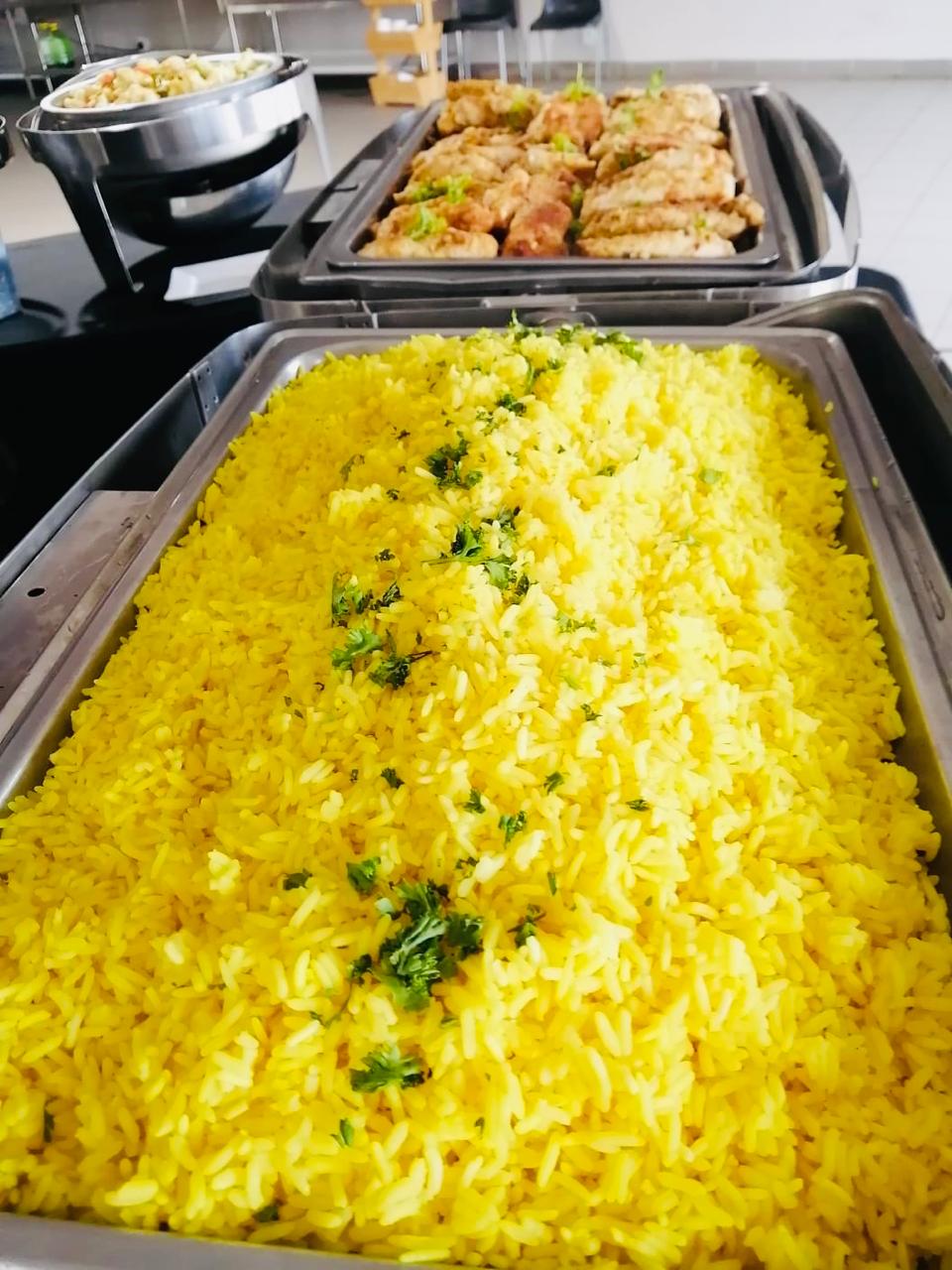 Full gastronorm trays of yellow rice and crumbed chicken on the hot line.
