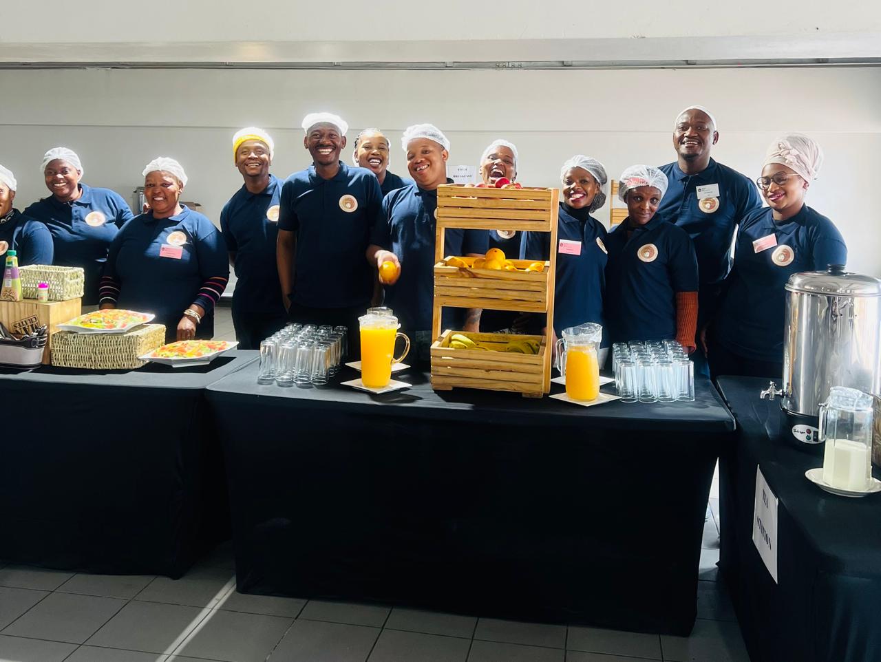 Abaholi team at a fruit and juice station, one member holding up an orange.